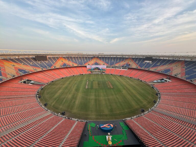 Empty cricket stadium during the day with bright daylight illuminating the green pitch and stands